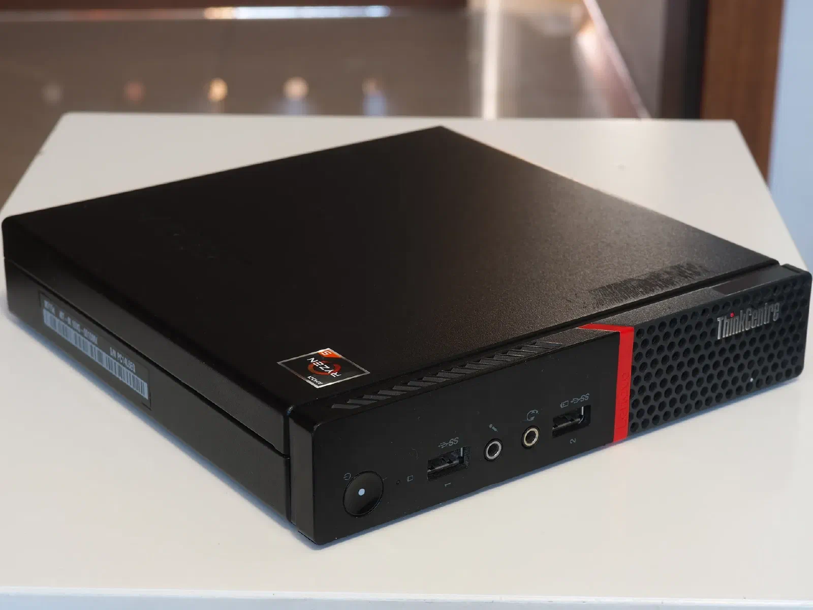 Lenovo ThinkCentre M715q Tiny, preto, sobre uma mesa branca